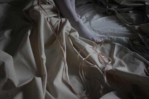 Close-up of Messy Bedsheets and Female Leg Wearing White Tights