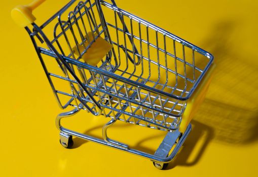 A close-up shot of a toy shopping cart on a bright yellow surface, ideal for retail or commerce themes.