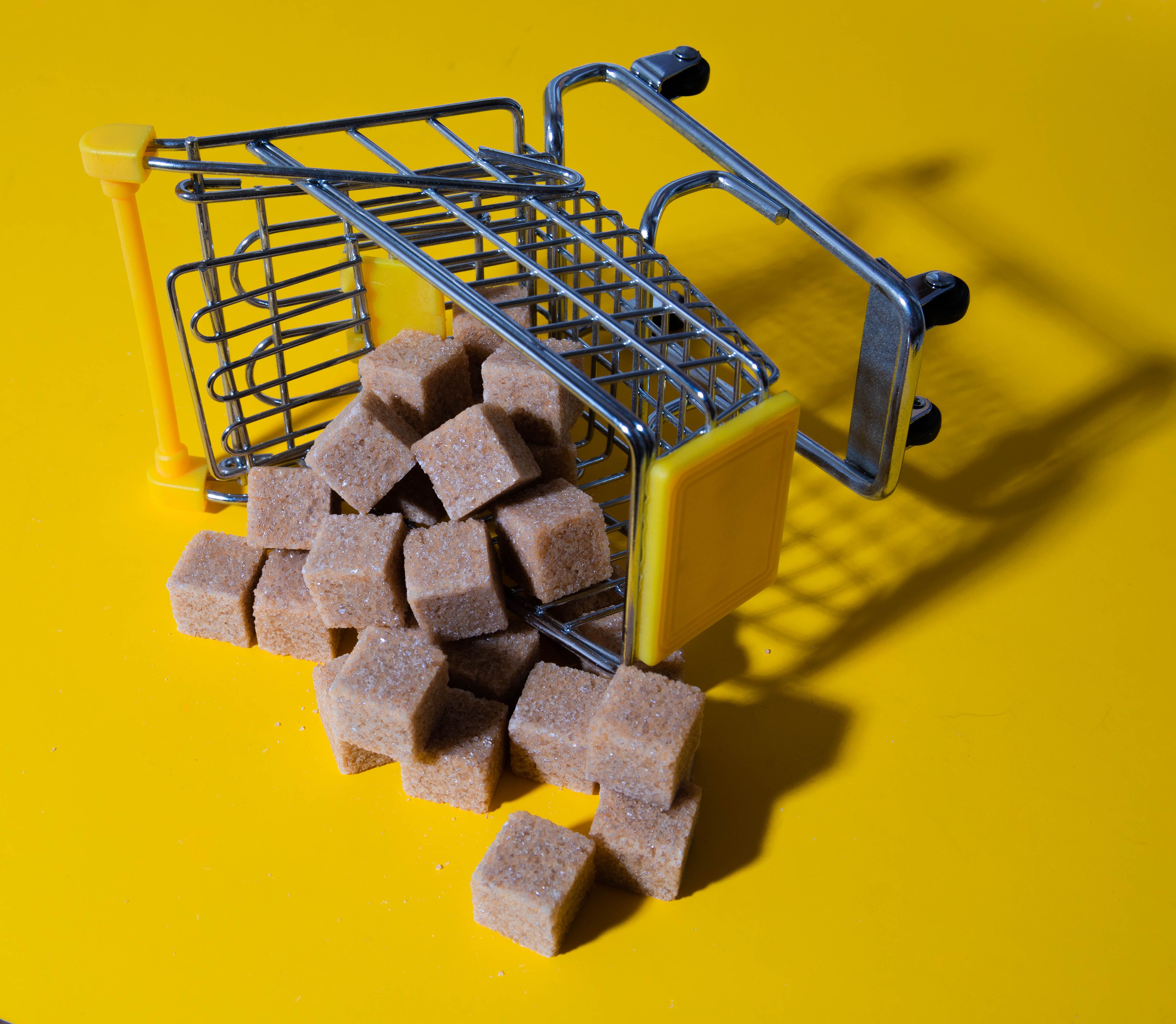 Brown sugar cubes spilling from a small shopping cart on a vibrant yellow background.
