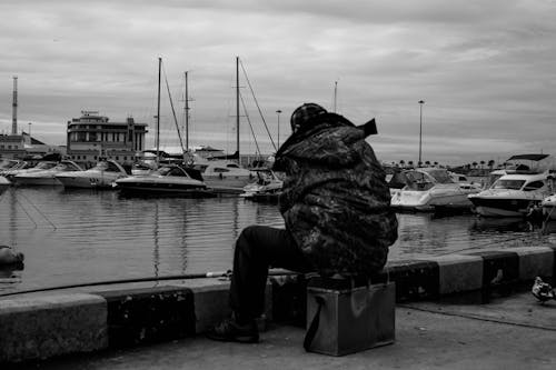 Grayscale Photo of a Person Fishing on a Harbor