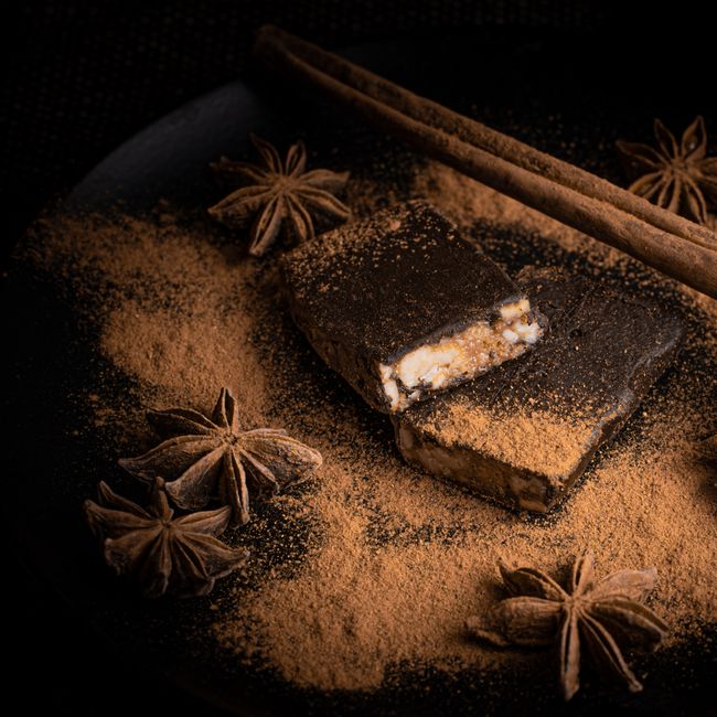 A small glass jar of reddish-brown Chinese five spice powder surrounded by whole star anise pods, cloves, fennel seeds, cinnamon sticks, and Sichuan peppercorns on a wooden board.