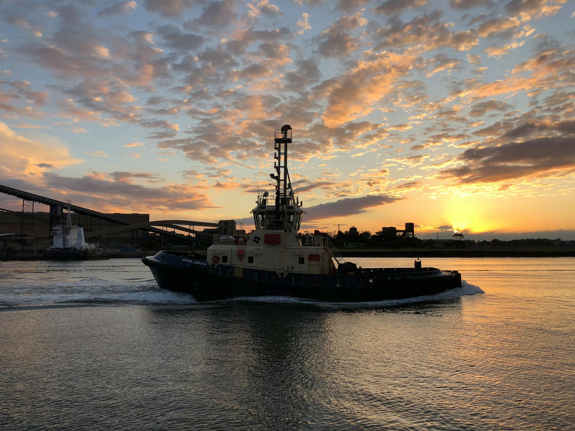 Tugboat navigating Hunter River with vibrant sunrise in Newcastle, Australia.