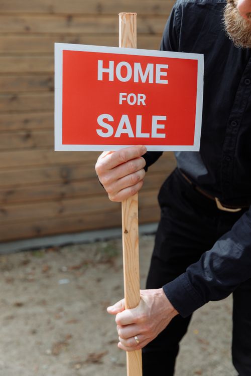 Free A person holding a red 'Home for Sale' sign outdoors in daytime, indicating real estate activity. Stock Photo