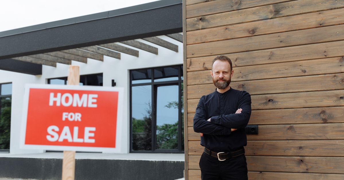 Real estate agent standing by a modern home with a 'Home for Sale' sign.