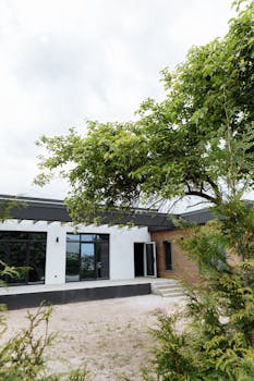 Contemporary house exterior featuring glass panels and greenery under a cloudy sky.
