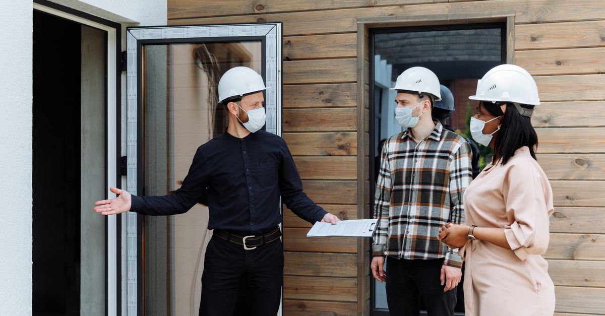 Real estate agent with clients viewing a new house during COVID-19 wearing safety gear.