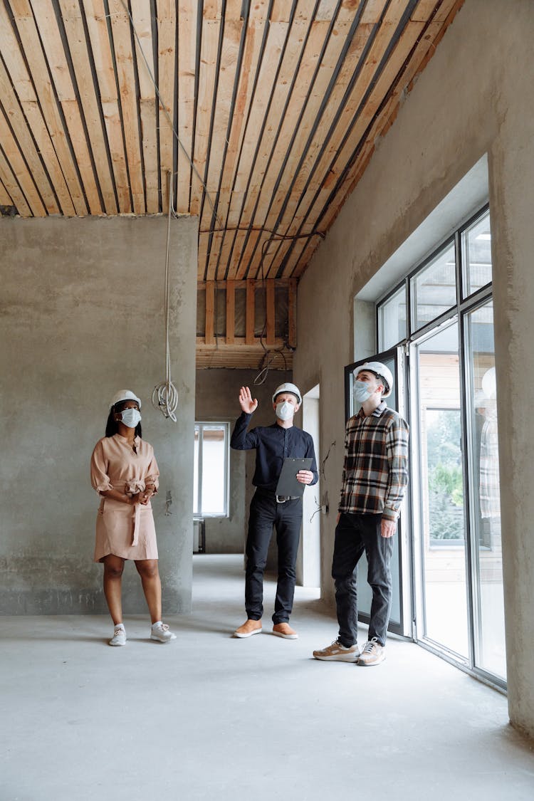 A Group Of People Standing Inside The House Talking While Wearing Face Masks And Hard Hats