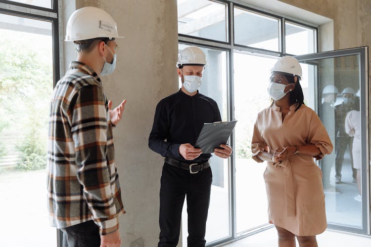 A Group Of People Wearing Face Mask And Hard Hats While Having Conversation