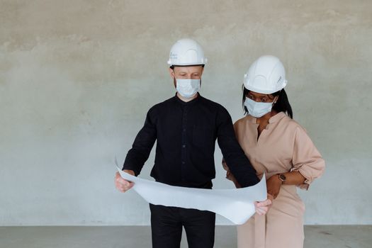 Engineers in safety helmets reviewing building plans indoors