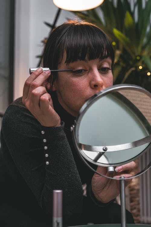 Free Woman Holding a Face Mirror Putting Eyeliner  Stock Photo