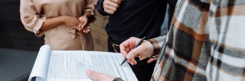 Three adults in an office setting discussing and signing a document.