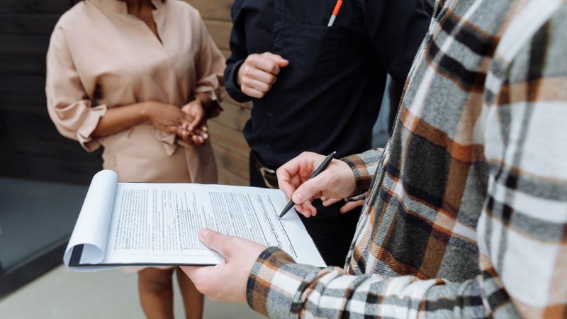 Three adults in an office setting discussing and signing a document.