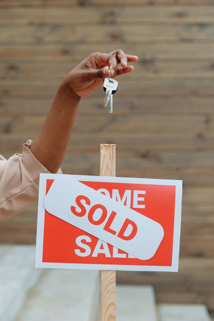 A Sold Signboard And A Person Holding Keys