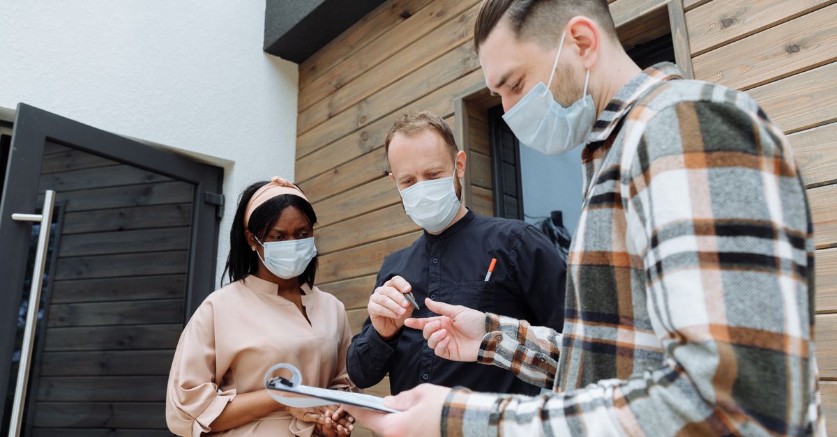 Three people in masks outside discussing paperwork during COVID-19 pandemic.