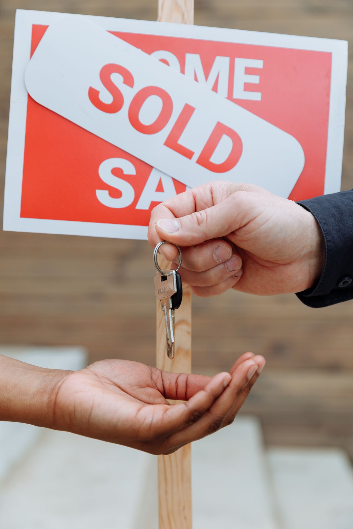 Keys being handed over in front of a sold sign