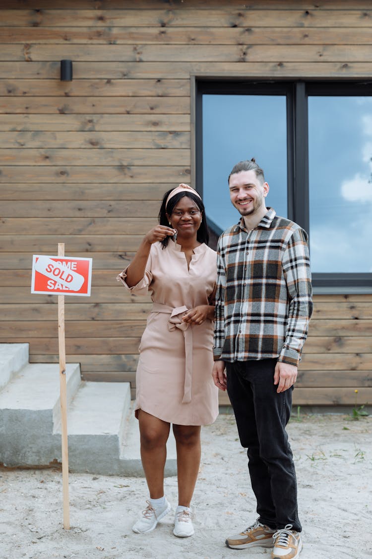 A Happy Couple Holding The Key Of A House While Smiling At The Camera