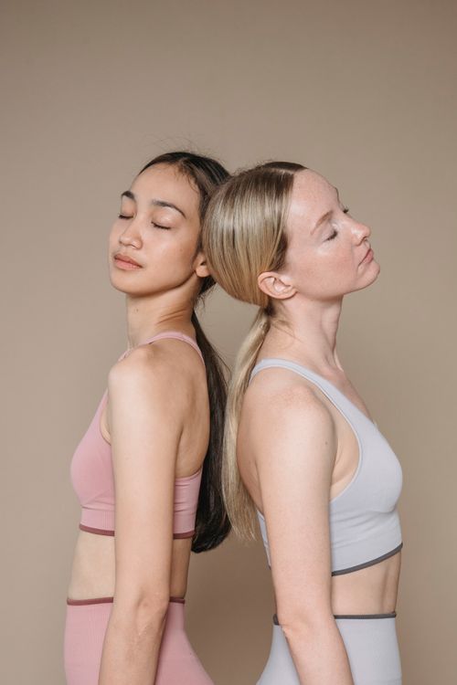 Free Two women in activewear with closed eyes posing back to back against a beige studio background. Stock Photo