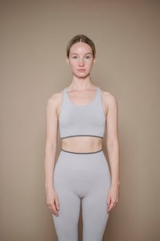 A woman in light activewear standing against a neutral background in a studio setting.