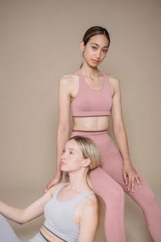 Two women in stylish sportswear pose gracefully in a minimalistic studio setting.