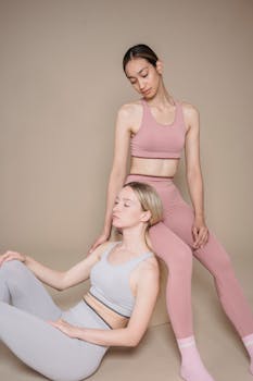 Two women in stylish pastel sportswear sitting gracefully in a studio, embodying calmness and poise.
