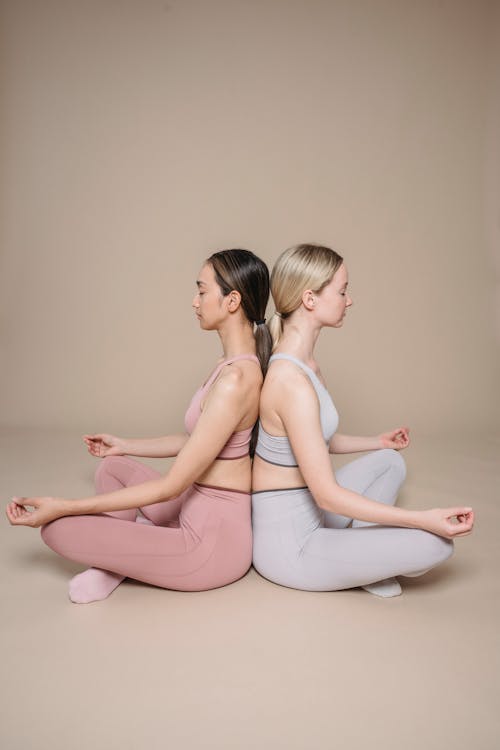 Free Women Sitting Back to Back while Doing Yoga Stock Photo