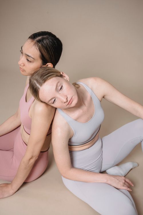 Free Two women in activewear sitting back to back on a studio floor, reflecting calmness. Stock Photo