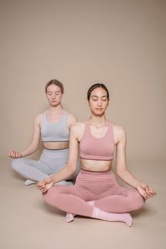 Two women practicing yoga meditation in a minimalist studio, eyes closed, focusing on inner peace.