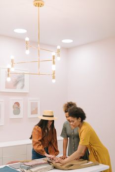 Three women in a modern office setting discuss fashion planning, showcasing teamwork and creativity.