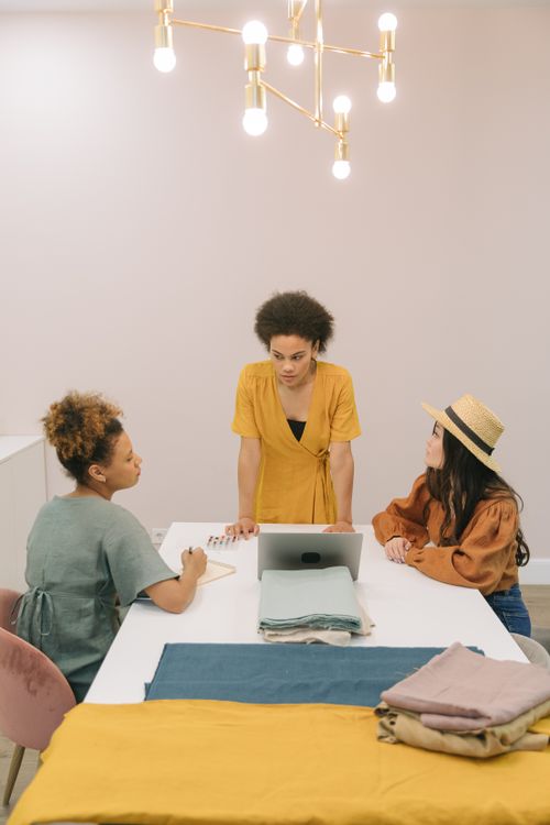 Free Three women engaged in a business meeting around a table with textiles. Stock Photo