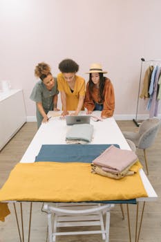 Three diverse fashion designers planning and discussing ideas around a table with fabrics and a laptop.