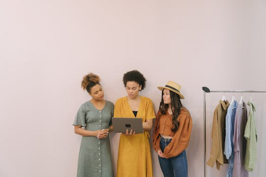Three women discuss business strategy in a fashion boutique with clothes on display.