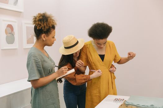 Three women collaborating on dress measurements in a fashion studio.