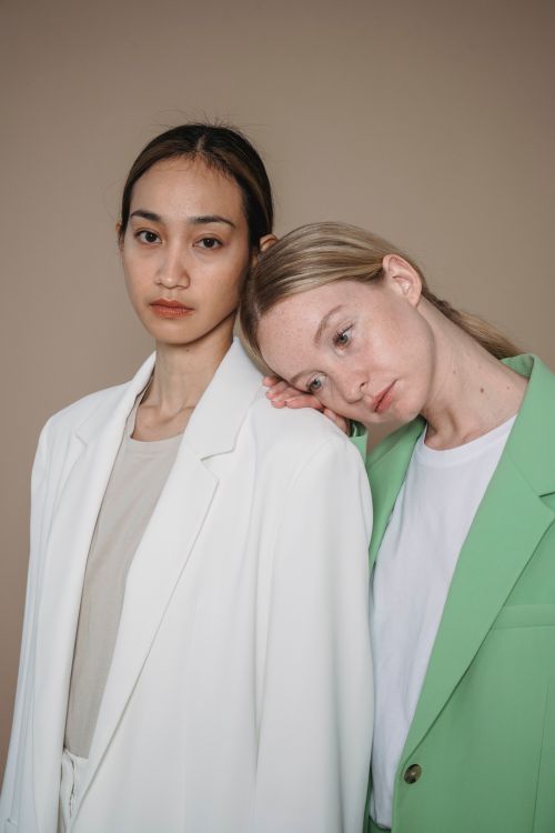 Free Portrait of two women in stylish blazers against a beige background, showcasing diversity and modern fashion. Stock Photo