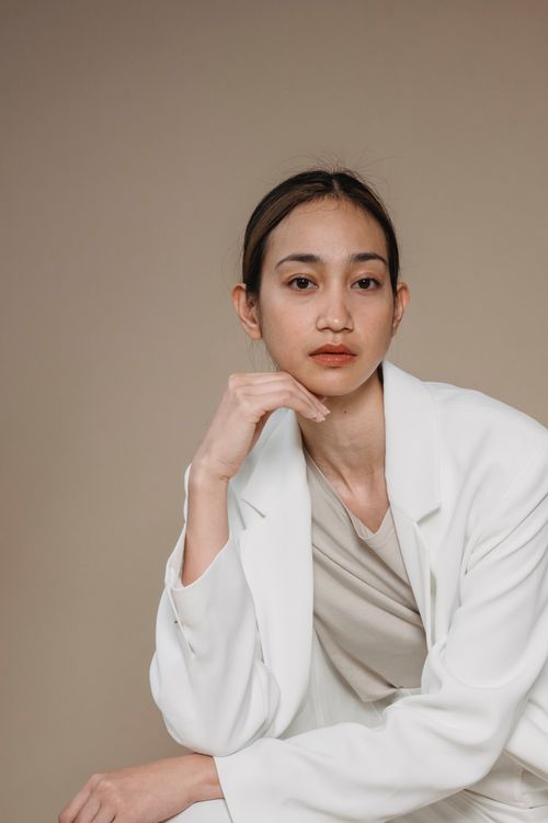 Free Studio portrait of an adult woman in a white blazer looking thoughtful with a hand on chin. Stock Photo