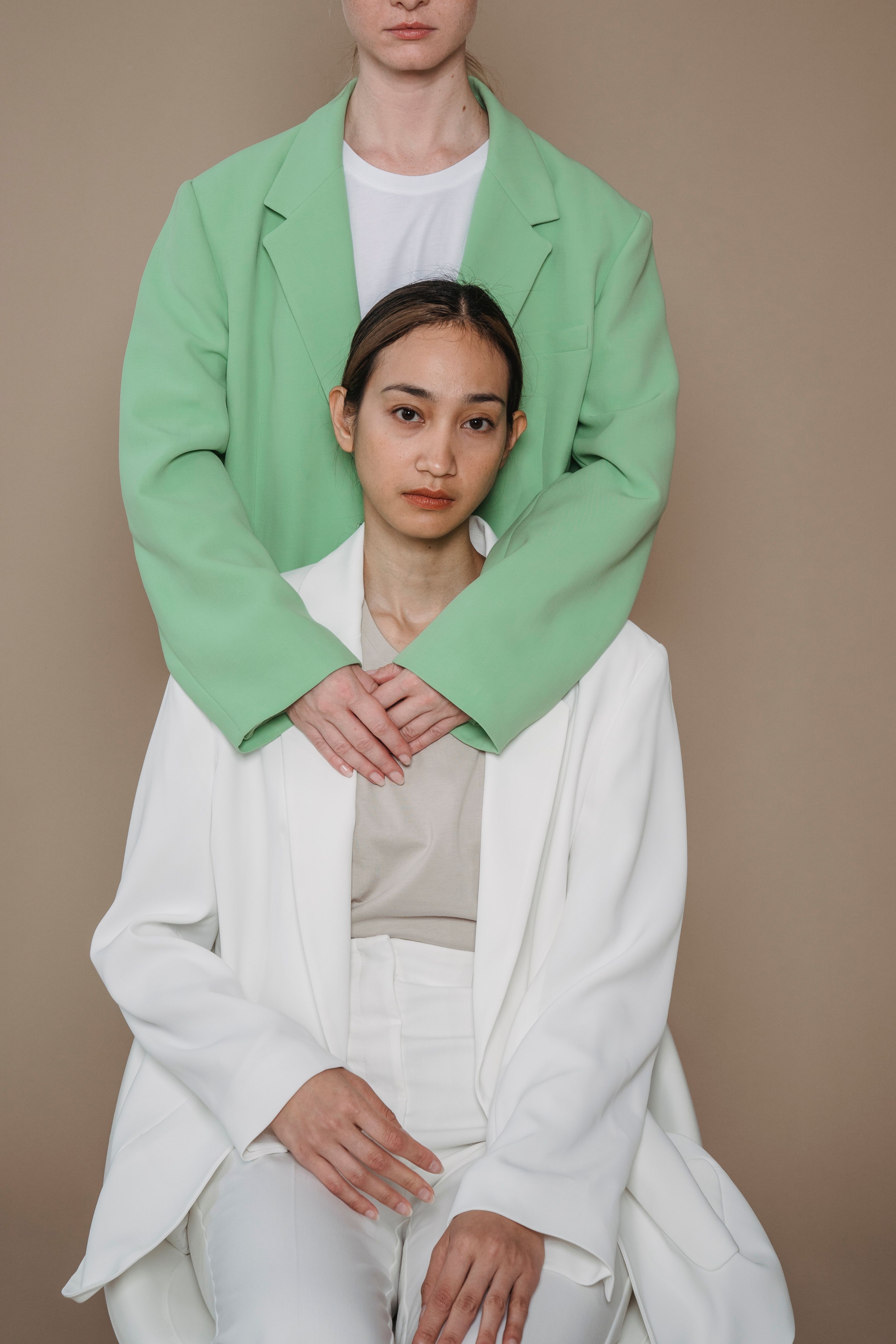 Duas mulheres em blazers estilosos posando elegantemente contra um fundo bege, mostrando a moda moderna.