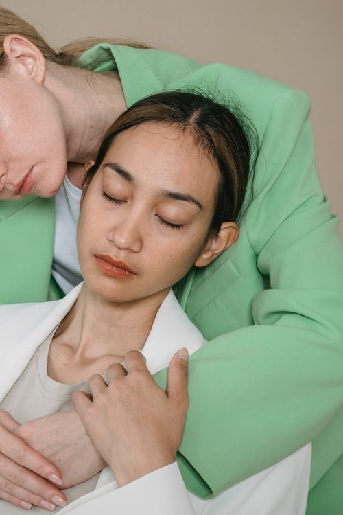 Free An intimate studio portrait of two women embracing while wearing green and white blazers, eyes closed. Stock Photo