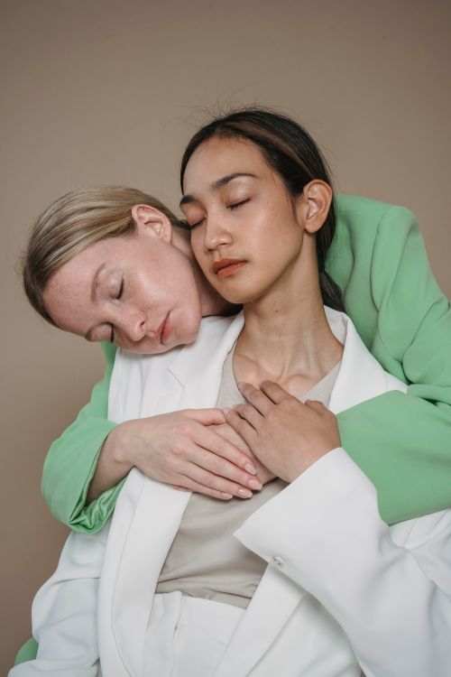 Free Portrait of two women embracing in a studio setting, wearing stylish blazers, eyes closed. Stock Photo