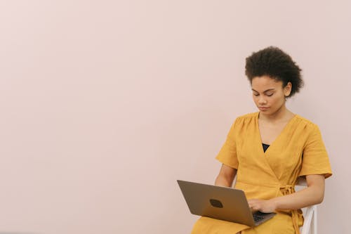 Free A Woman in Yellow Dress Sitting while Using Her Laptop Stock Photo