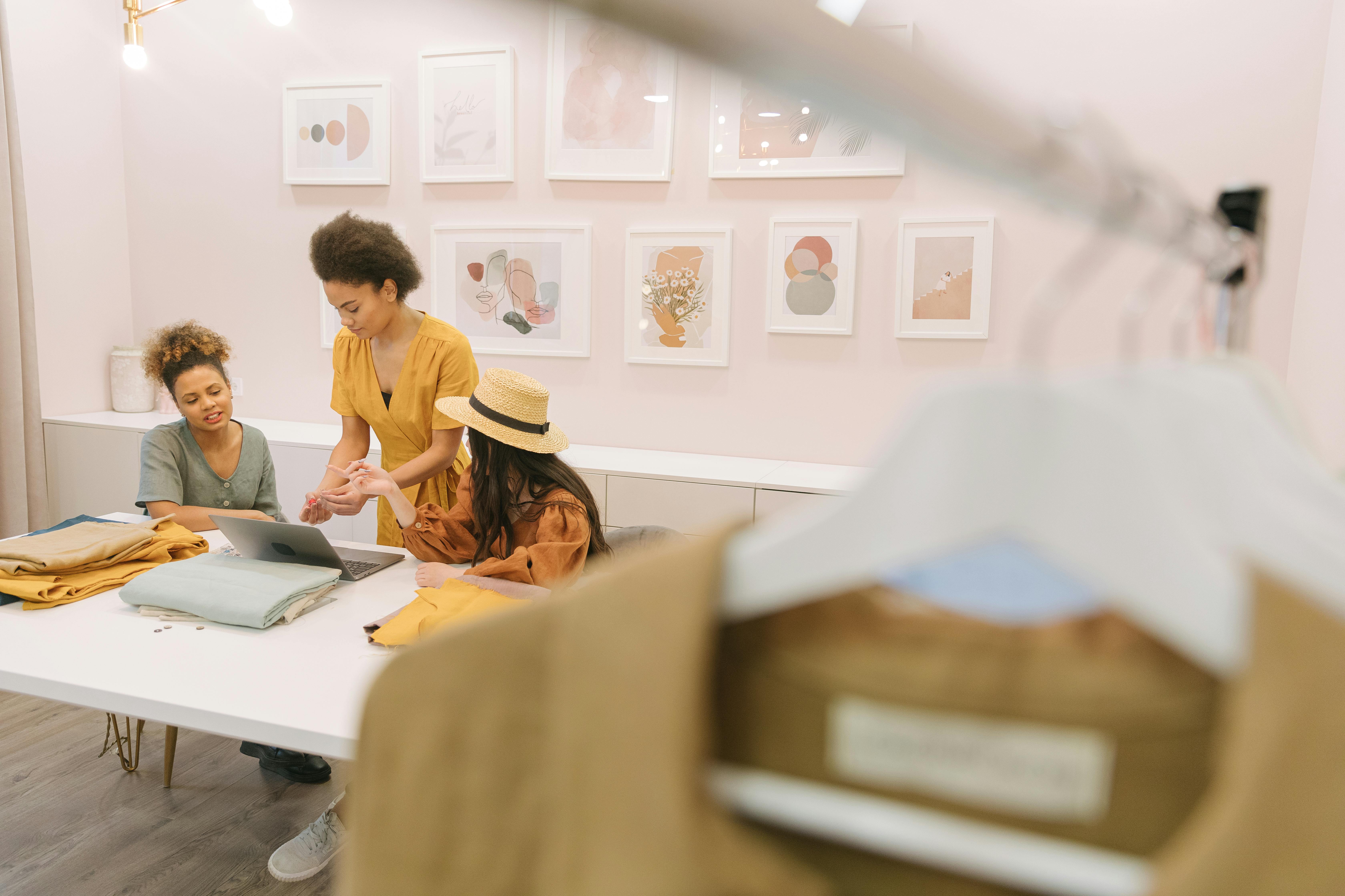 Three women engaged in brainstorming session with fabrics and laptop in a stylish fashion studio.