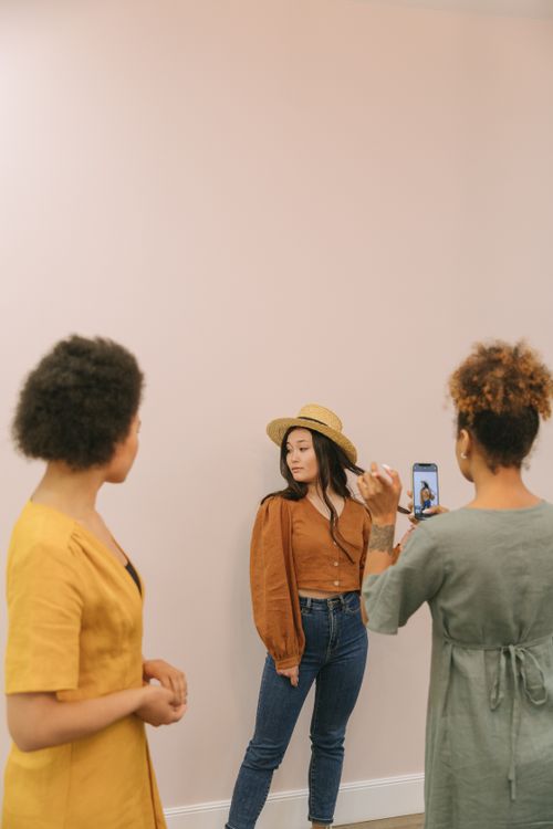 Free Three women in stylish attire during a playful indoor photoshoot, using a smartphone. Stock Photo