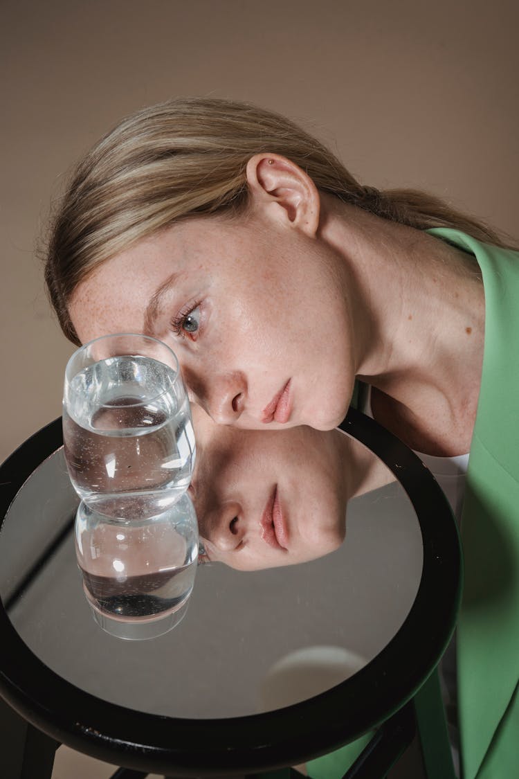 Woman Looking Intensely At Glass Of Water Reflecting In Mirror