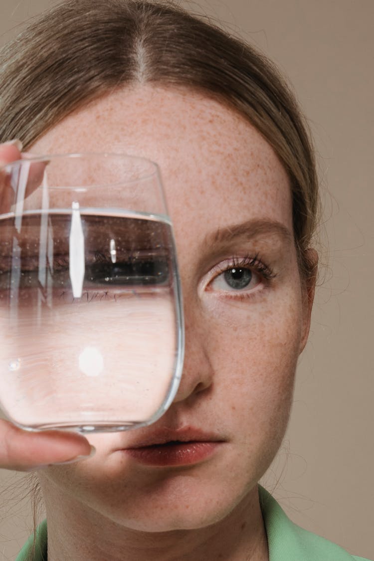 Woman Covering Her Eye With A Clear Drinking Glass With Liquid 