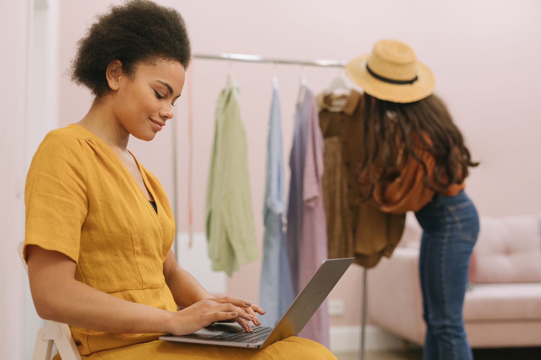 Woman in yellow dress working on laptop in small fashion boutique.