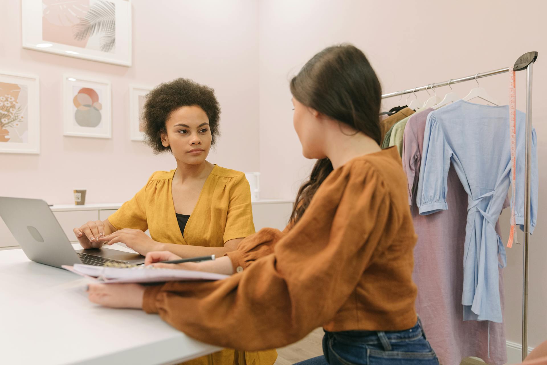 Two women discussing a fashion business strategy indoors with clothing rack.