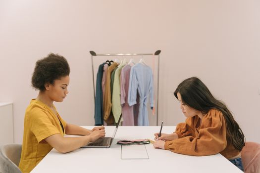 Two women working together in a fashion design office, focused on a project.