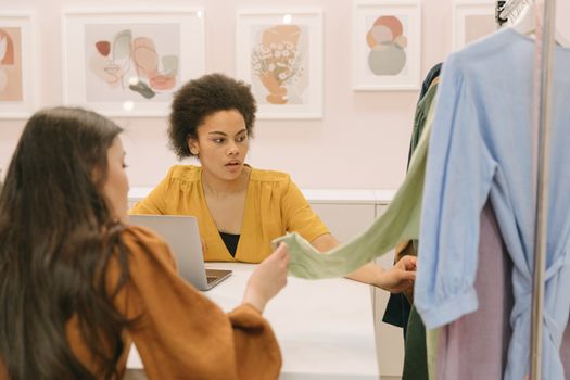 Two women collaborate in a modern fashion design setting, reviewing fabric choices.