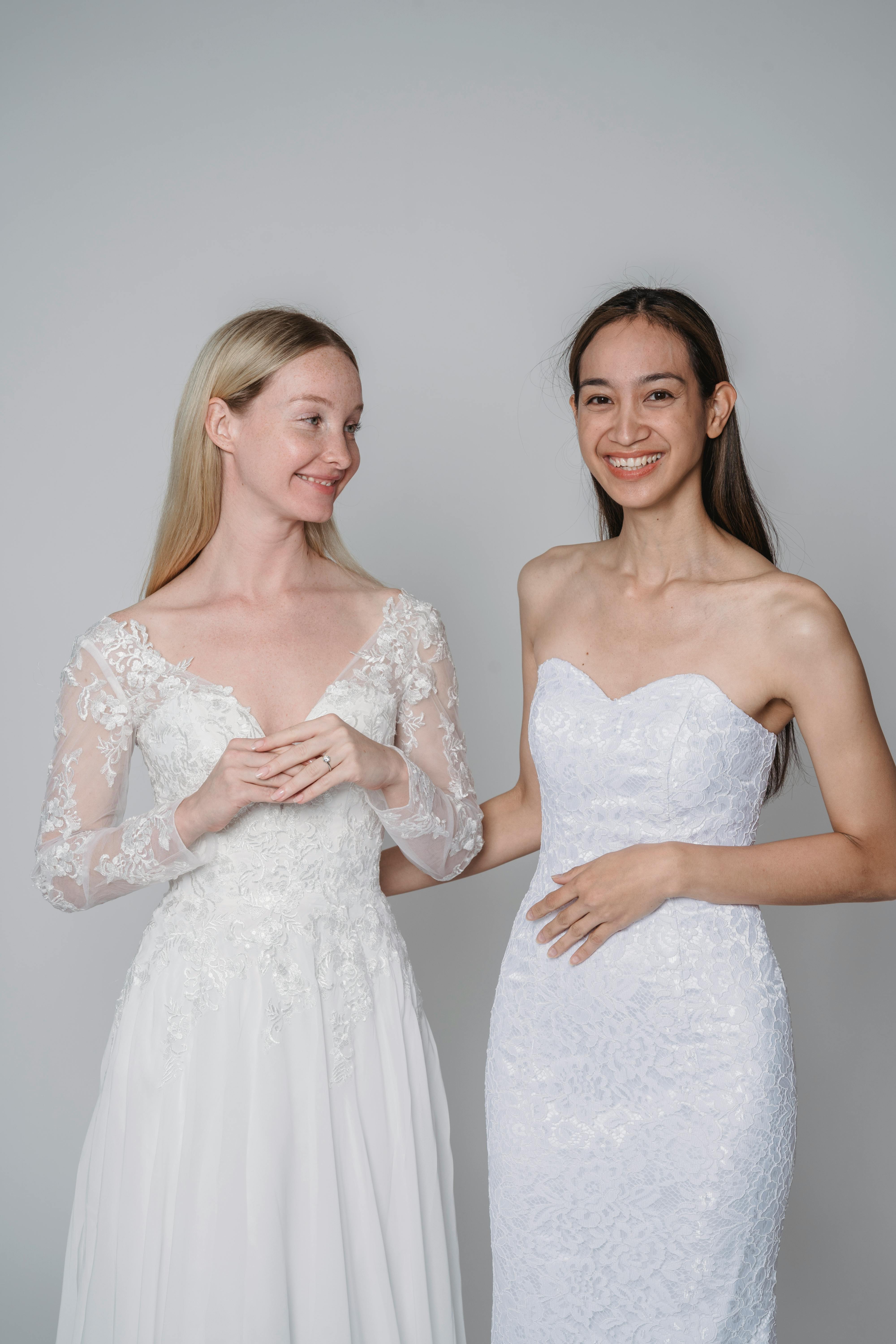 Two women in bridal dresses smiling in a studio shoot, showcasing elegance and modern fashion.