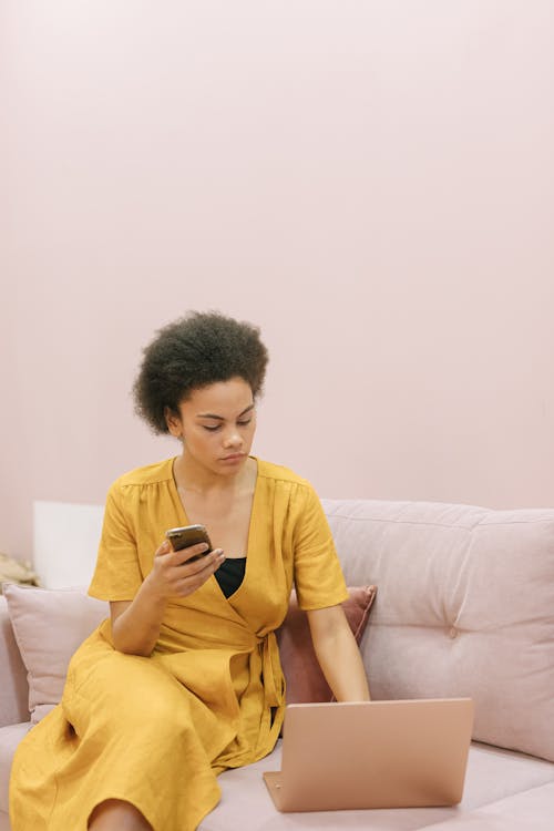 Free Woman in Yellow Dress Sitting on Sofa while Using Laptop Stock Photo