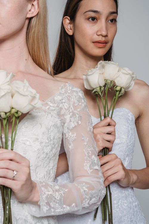 Free Two brides in delicate wedding dresses hold white roses, creating a sophisticated bridal scene. Stock Photo