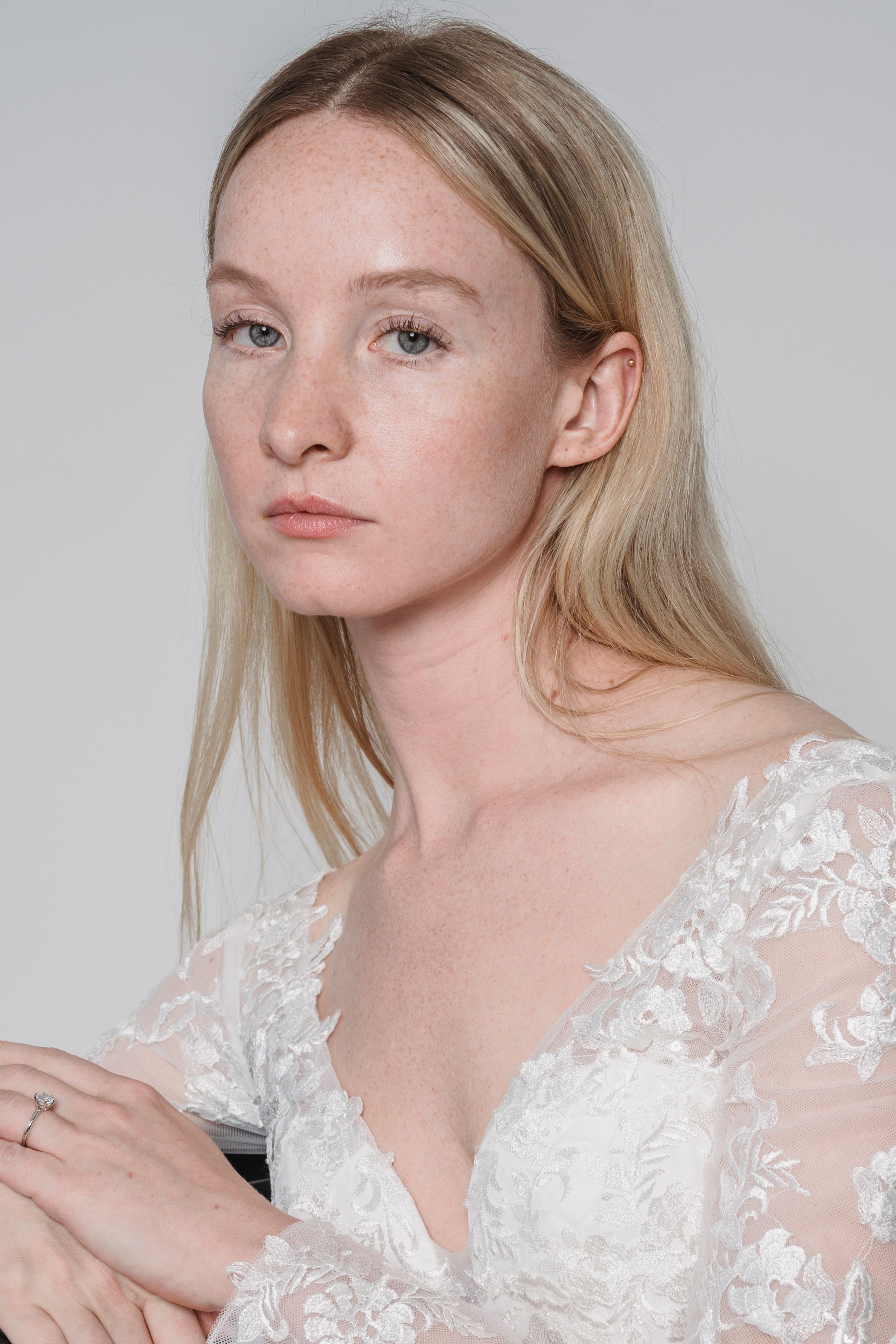 Serene portrait of a blonde woman in an elegant lace dress against a neutral background.